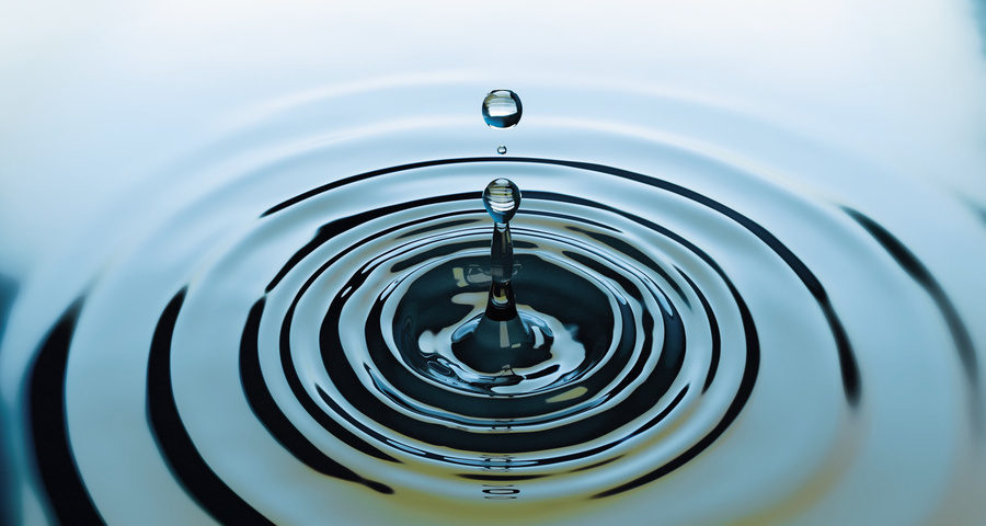 A water droplet sending ripples across a still pool